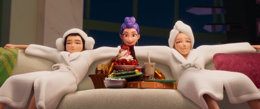 Kpop Demon Hunters Mira and Zoey in robes on a white couch with food between them and Rumi's head with her purple hair.