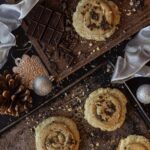Two baking trays hold a few brownish sugar cookies with peppermint topping.