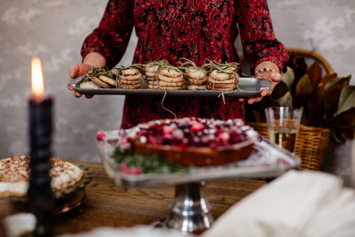 Rosemary Butter Cookies A woman holds out a tray of stacked Rosemary Butter Cookies while a cranberry cake sits in front of it.