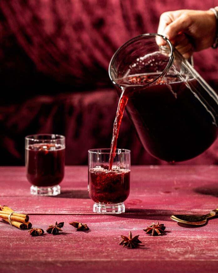 A pitcher filled with a dark red sangria cocktail garnished with cinnamon sticks and star anise pods, as described in the recipe for the 