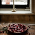 A spiced mascarpone cranberry cake sits below a window sill with a candle on it.