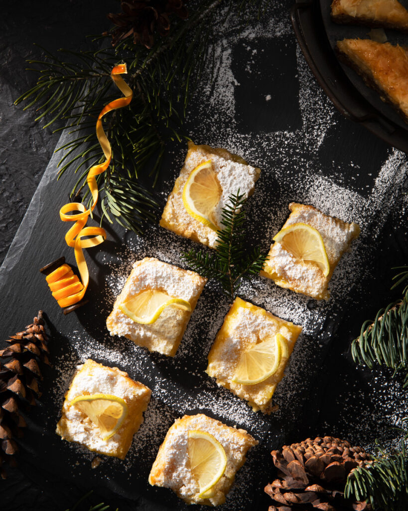 Lemon bars on a black tabletop, covered in powdered sugar