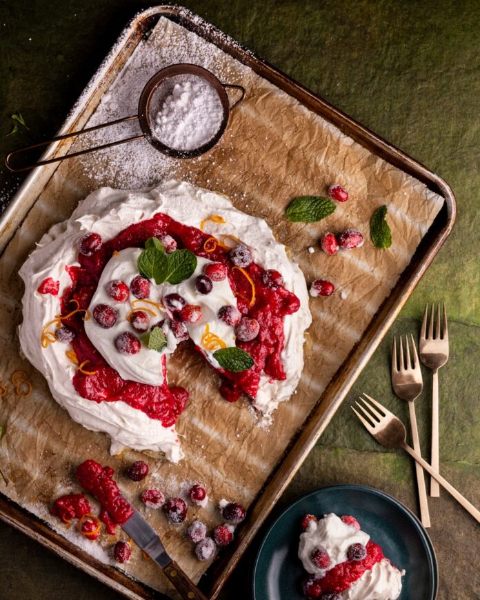 A freshly prepared winter white pavlova dessert with whipped cream, berry compote, and mint garnish.
