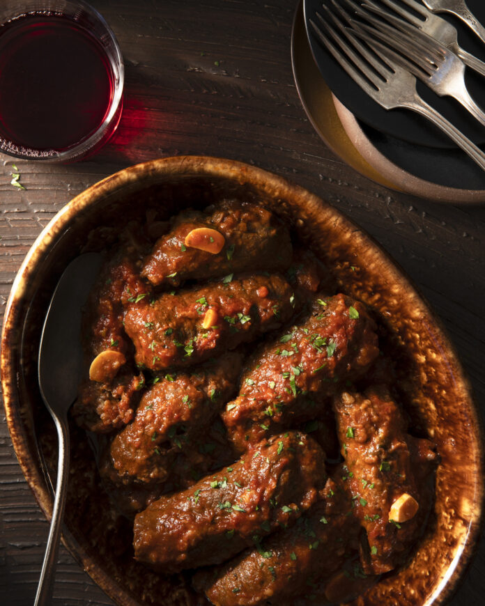 A bowl filled with braciole, featuring meat and sauce, elegantly presented on a dining table.