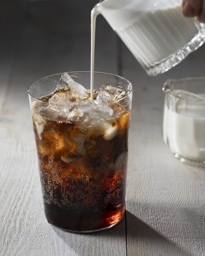 A glass of cherry coke dirty soda filled with a deep red, fizzy beverage, with ice cubes and a cherry garnish floating in the liquid.