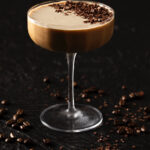 A chocolate espresso martini staged on a black background with a dusting of espresso bean on the top