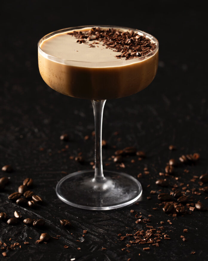 A chocolate espresso martini staged on a black background with a dusting of espresso bean on the top