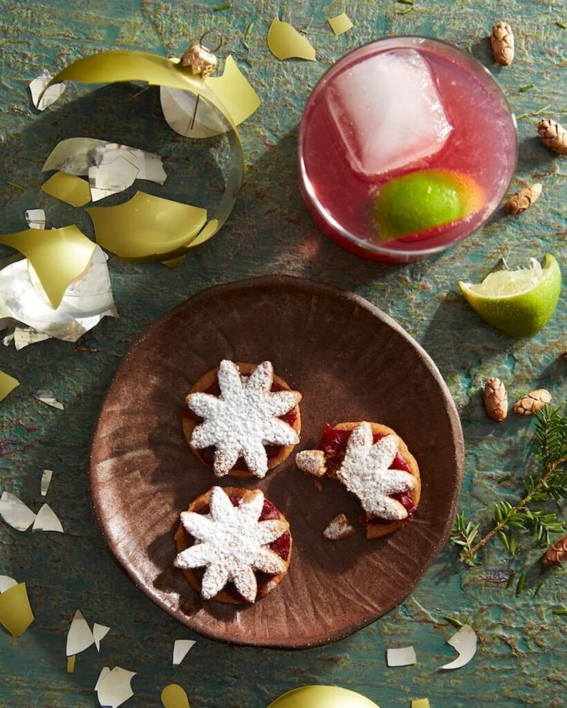 Chrisma Politan Cocktail with a twist of citrus and a touch of elegance, garnished with fresh cranberries and a sprig of rosemary.