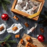 A glass box with wood edges holds wrapped caramels inside while unwrapped Ear Gray Salted Caramels sit below it on a black background beside a tee branch holding a red ornament.