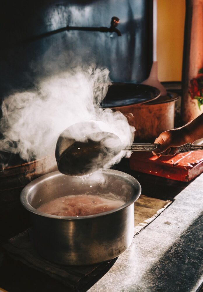 A sizzling pot on a stove, steam coming off of a ladle in a cozy-looking kitchen
