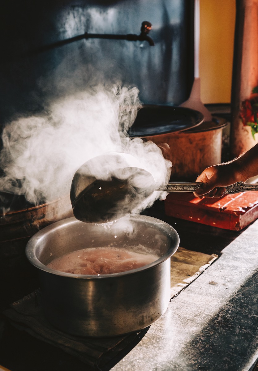A sizzling pot on a stove, steam coming off of a ladle in a cozy-looking kitchen
