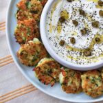 A plate of Greek Zucchini fritters with a hefty dish of yogurt sauce with capers