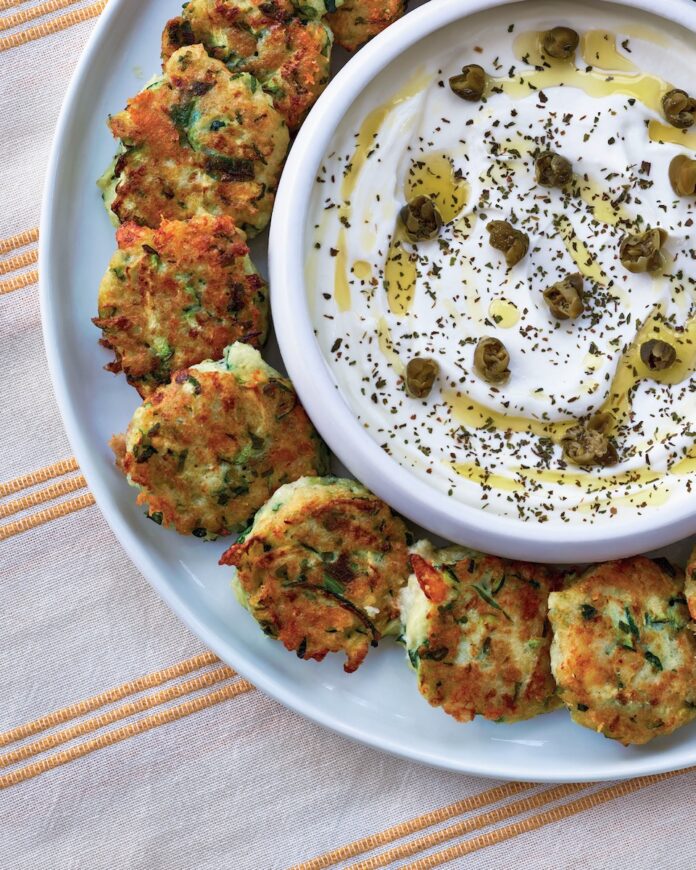 Greek Zucchini Fritters A plate of Greek Zucchini fritters with a hefty dish of yogurt sauce with capers