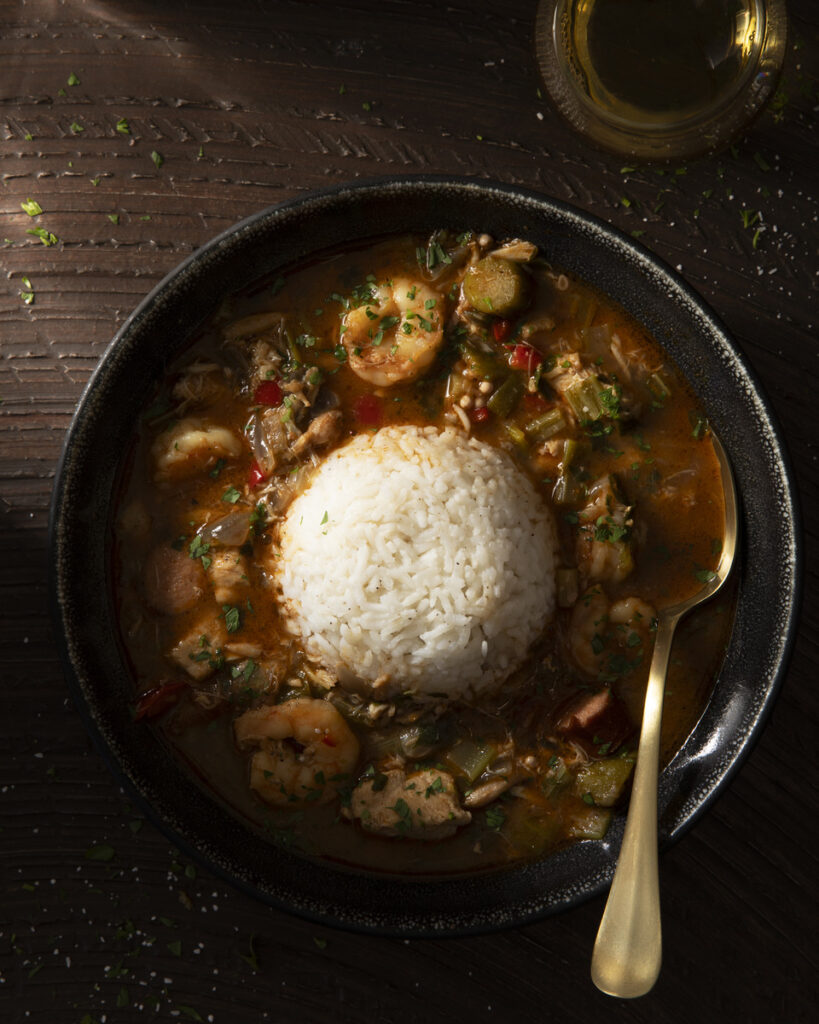 A bowl of hearty stew featuring rice, vegetables, and a medley of seafood, including shrimp and crab meat.