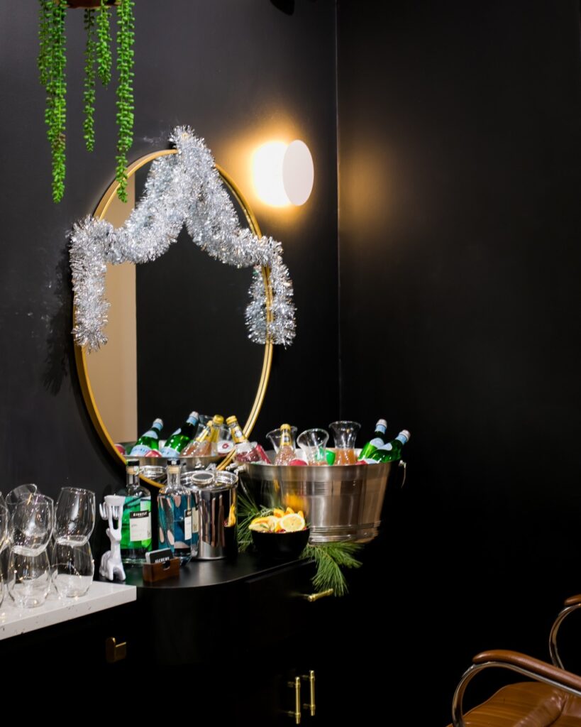 In the distance sits a table with buckets of beverages, glasses, and ice in front of a decorated round mirror.