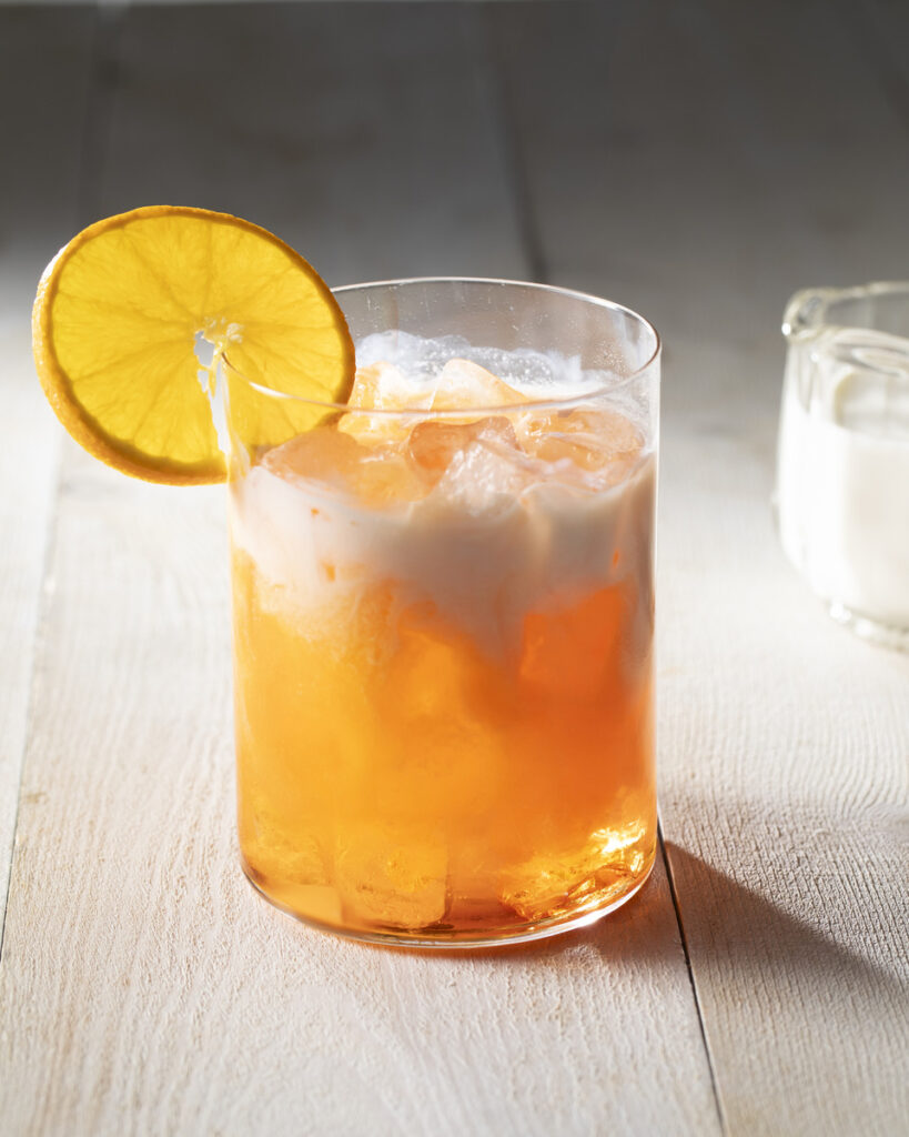 A glass filled with dirty orange soda, garnished with a slice of orange.