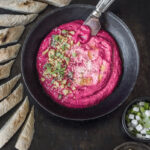 A pink bowl of beet and yogurt mousse with garnish on top of it