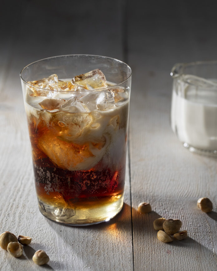 A glass filled with a dark, bubbly rootbeer-colored beverage, with ice cubes floating in the liquid.