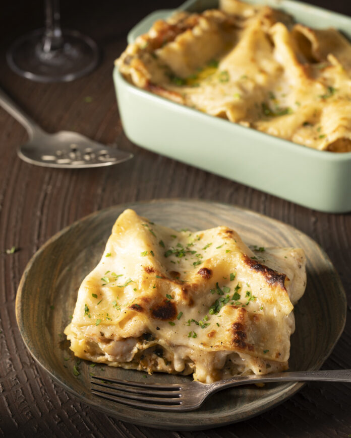 A delicious seafood lasagna on a plate, served with a fork and a glass of wine, showcasing a gourmet dining experience.