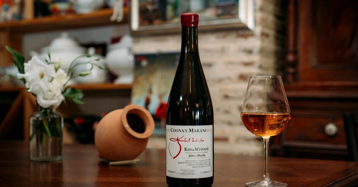 A clay jar, a bottle of wine, and a glass of amber wine sit on a table at Georgian winery Chona's Marani