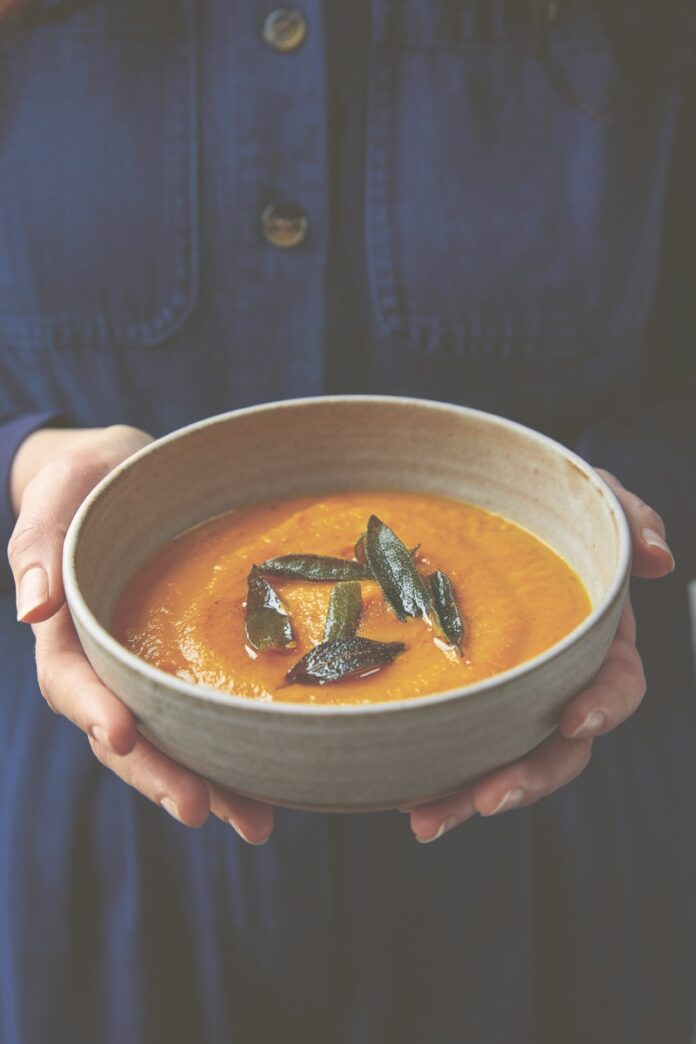 Delicata soup, garnished with time, held in the hands of a welcoming cook