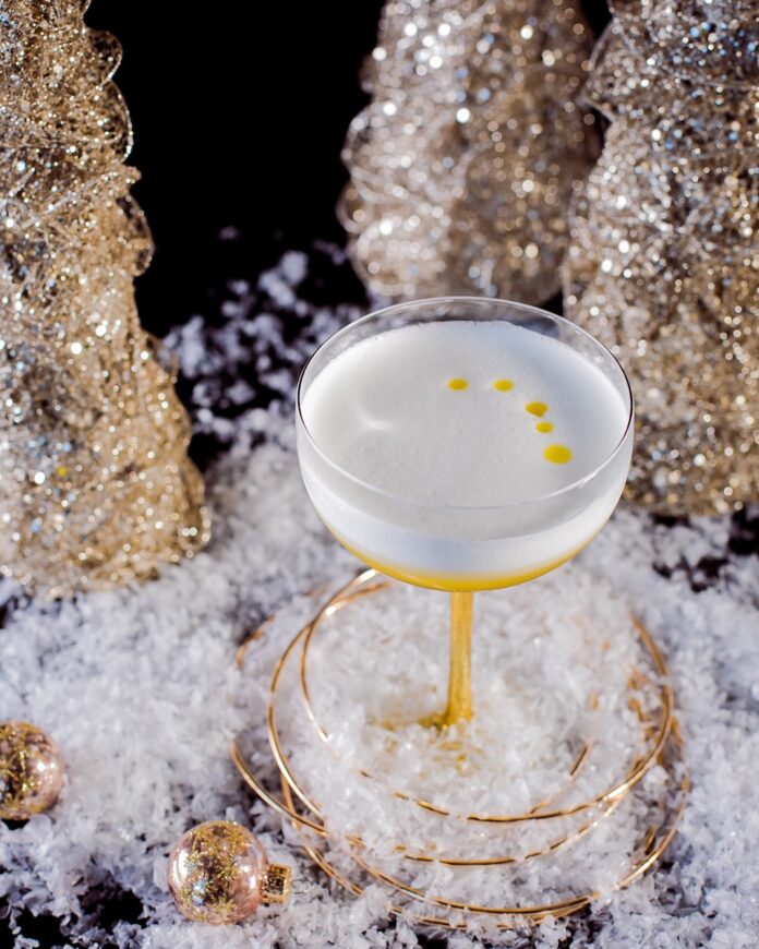 A limoncello cocktail with five drops of olive oil in it, staged with golden Christmas ornaments