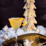 A nick and nora glass with a bright yellow Aviation cocktail in it