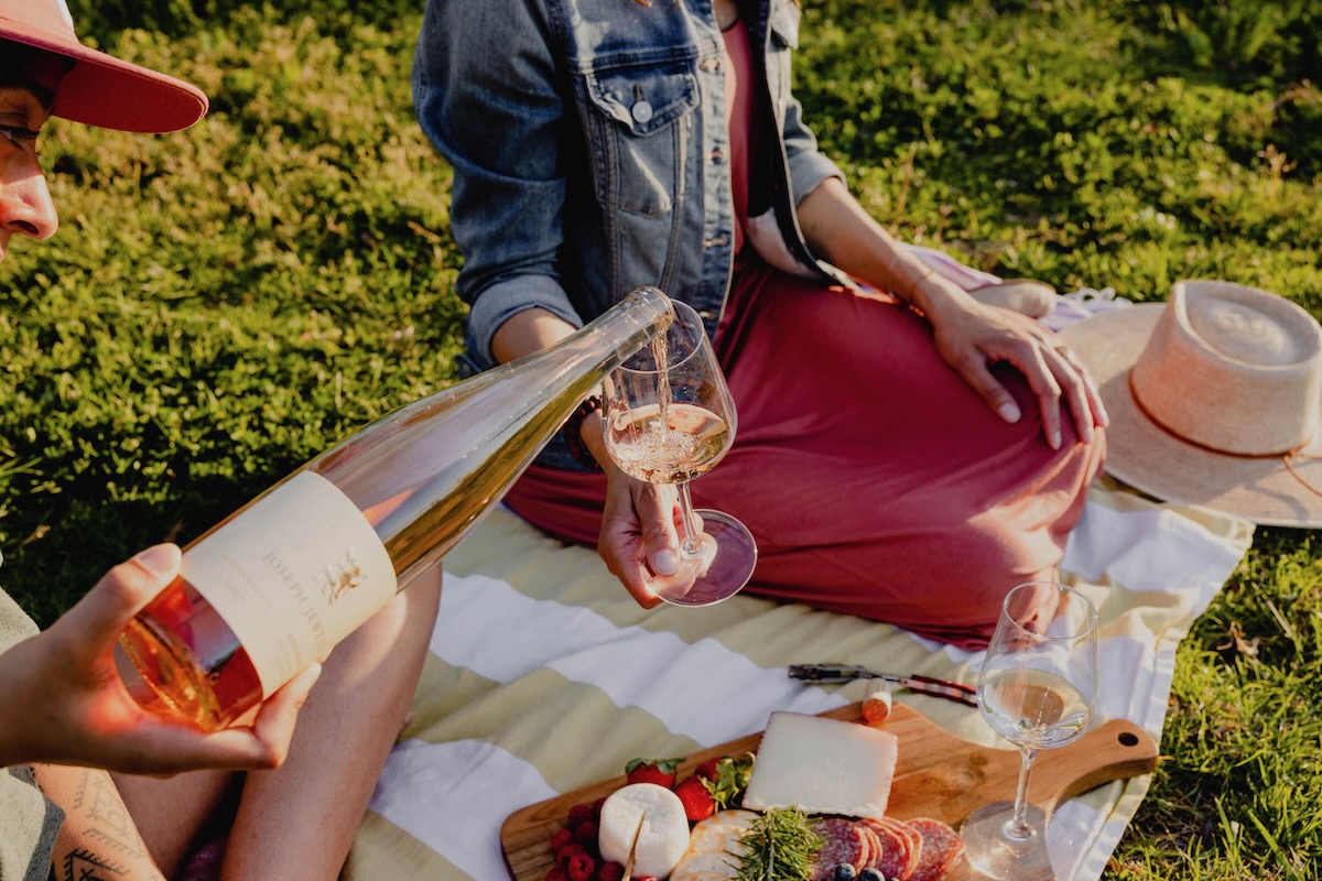 A bottle orange wine is poured into a glass at a sunny outdoor picnic