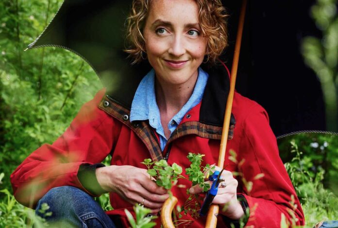 Karyn Tomlinson Chef Karyn Tomlinson stands in a garden, holding vegetables in her hand while wearing a red raincoat