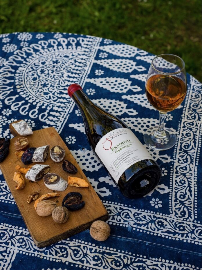A bottle of Georgian wine by Chona's Marani lays on a blue and white picnic blanket beside a cheese board
