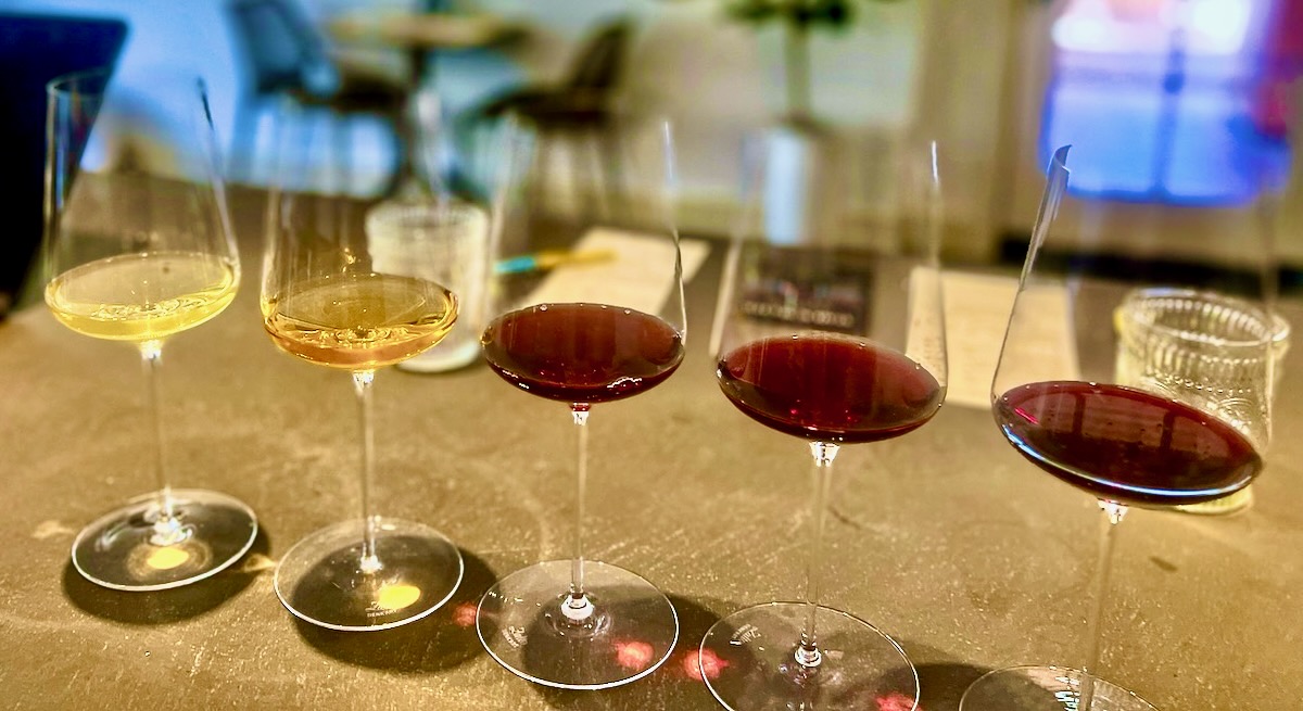 A lineup of wine glasses in the tasting room of Extradimensional Wine Co Yeah!, staged from pale lemon yellow to a dark garnet red