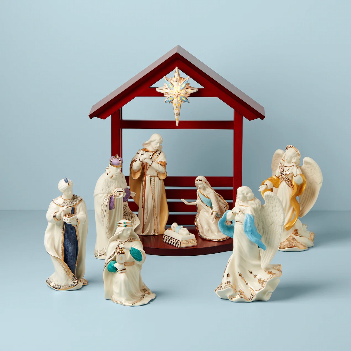 A scene of white nativity figures on a light blue background with a red créche