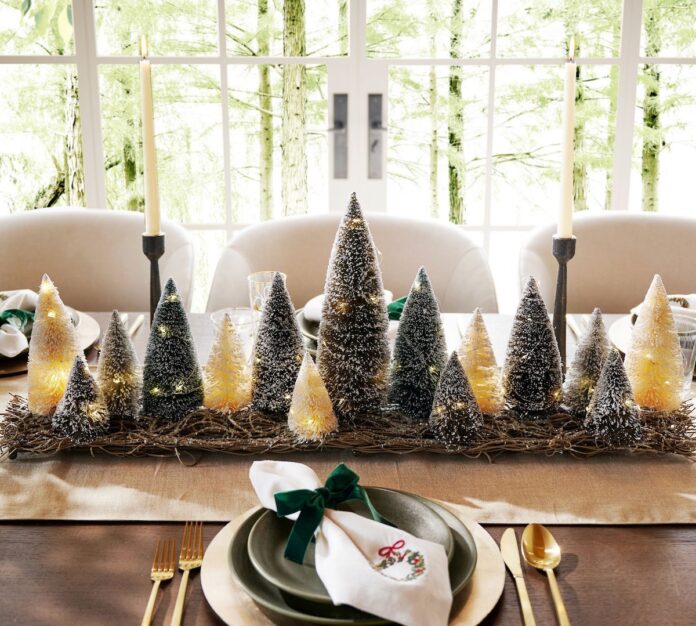A display of Christmas decorations from Pottery Barn, including small trees and a plate set with a napkin and green bow