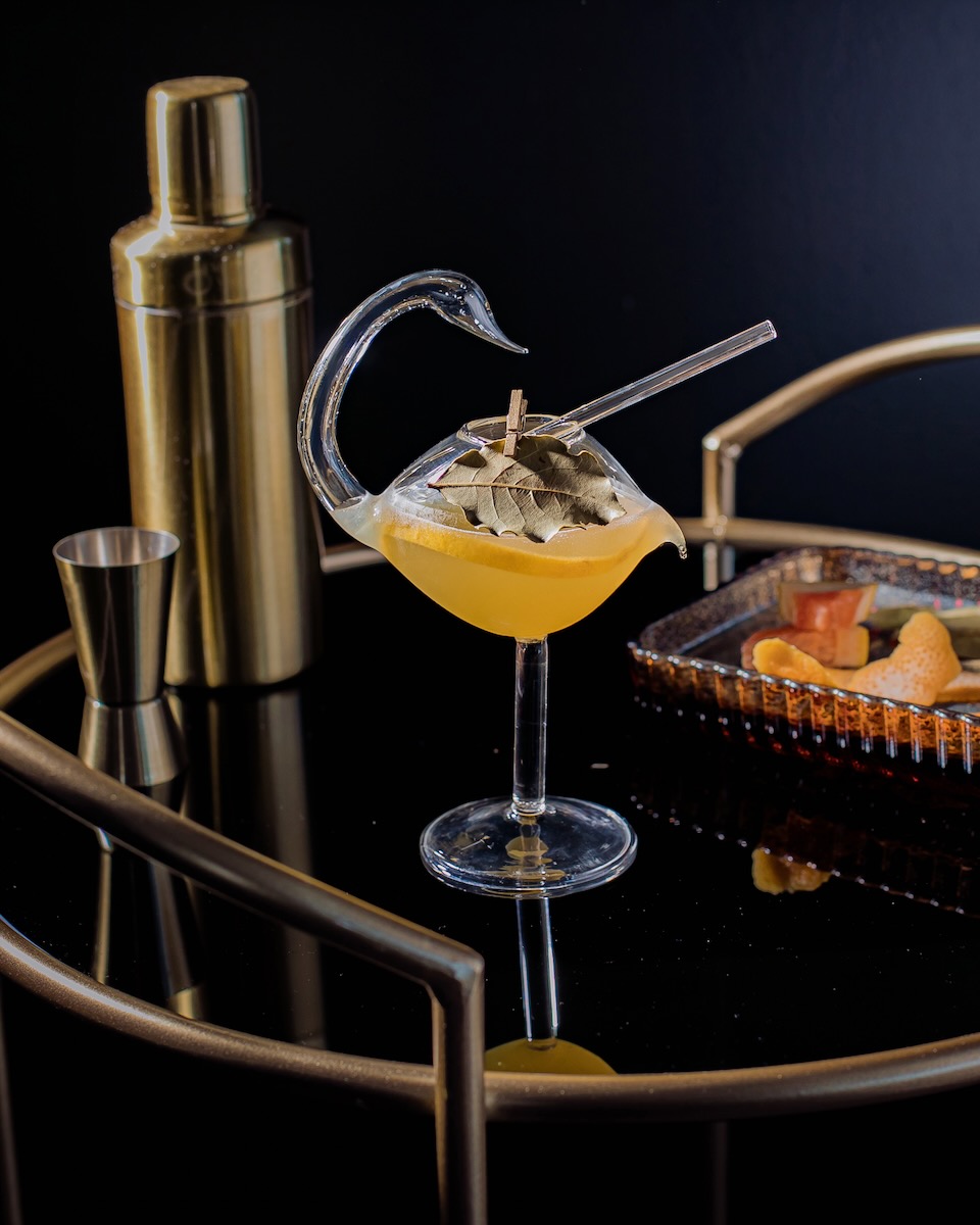 A swan-shaped glass holds a Hemingway daiquiri on a black background