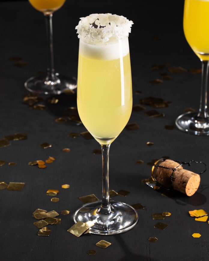 A champagne flute on a black background, topped off with coconut flakes and surrounded by festive decor