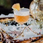 A ten-apple fan sits in an orange apple bourbon cocktail with a thick layer of foam, staged for Christmas
