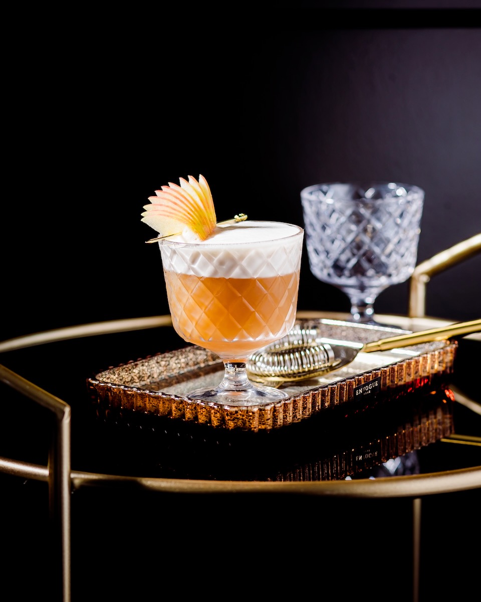 An apple bourbon cocktail with an apple slice fan in it on a black background