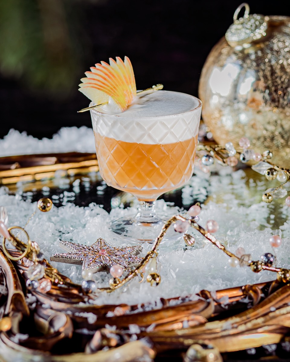 A ten-apple fan sits in an orange apple bourbon cocktail with a thick layer of foam, staged for Christmas