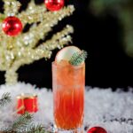 A red rum cocktail on a Christmas set dusted with artificial snow beside a golden Christmas tree