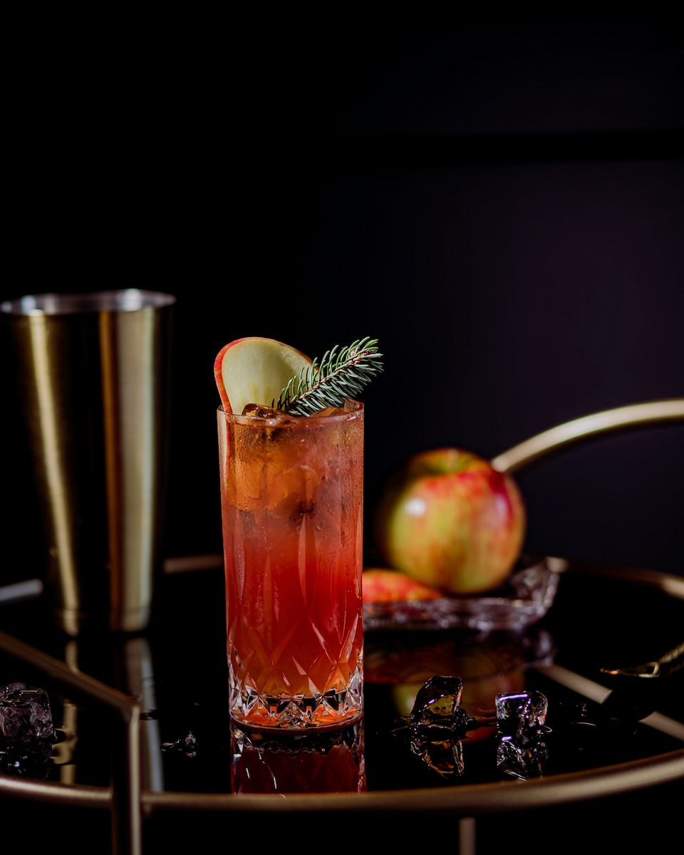 An easy rum cocktail with an apple wheel garnish staged on a black background
