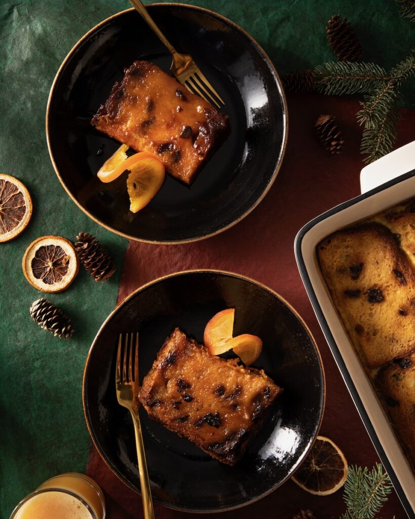 Two black bowls hold two slices of creme brulee french toast made with panettone with candied orange slices beside them.