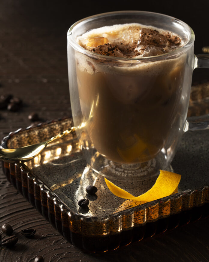 Gentleman’s Brew Non-Alcoholic Irish Coffee A glass mug filled with a dark, creamy-looking A non-alcoholic Irish coffee garnished with a lemon peel and what appears to be coffee beans or espresso grounds.