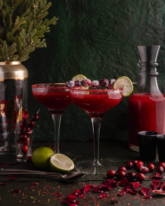 Three cranberry margaritas garnished with lime and staged for a Christmas table