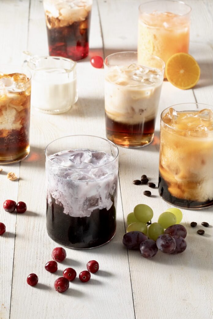 TABLE Magazine We made six dirty sodas to try the trend SIx dirty sodas arranged on a white wooden slatted surface with cranberries, grapes, coffee beans, hazelnuts and cherries as garnish on the surface.