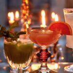 Two tequila cocktails, one red and one green, sit beside each other on a candlelit table
