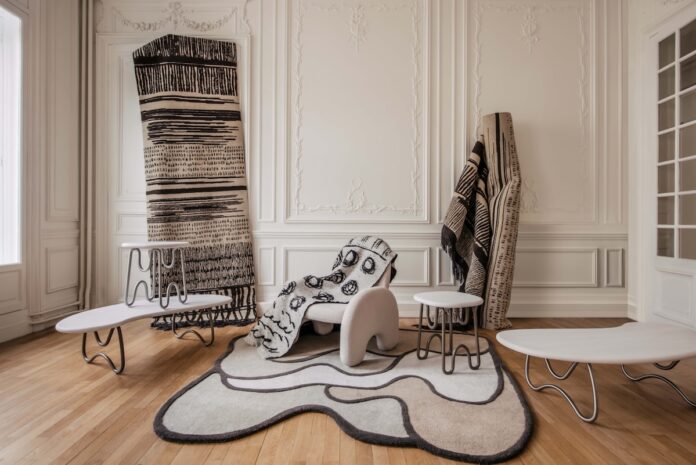 An interior by Faye Toogood with a white, wavy-shaped rug and white walls on a beige floor