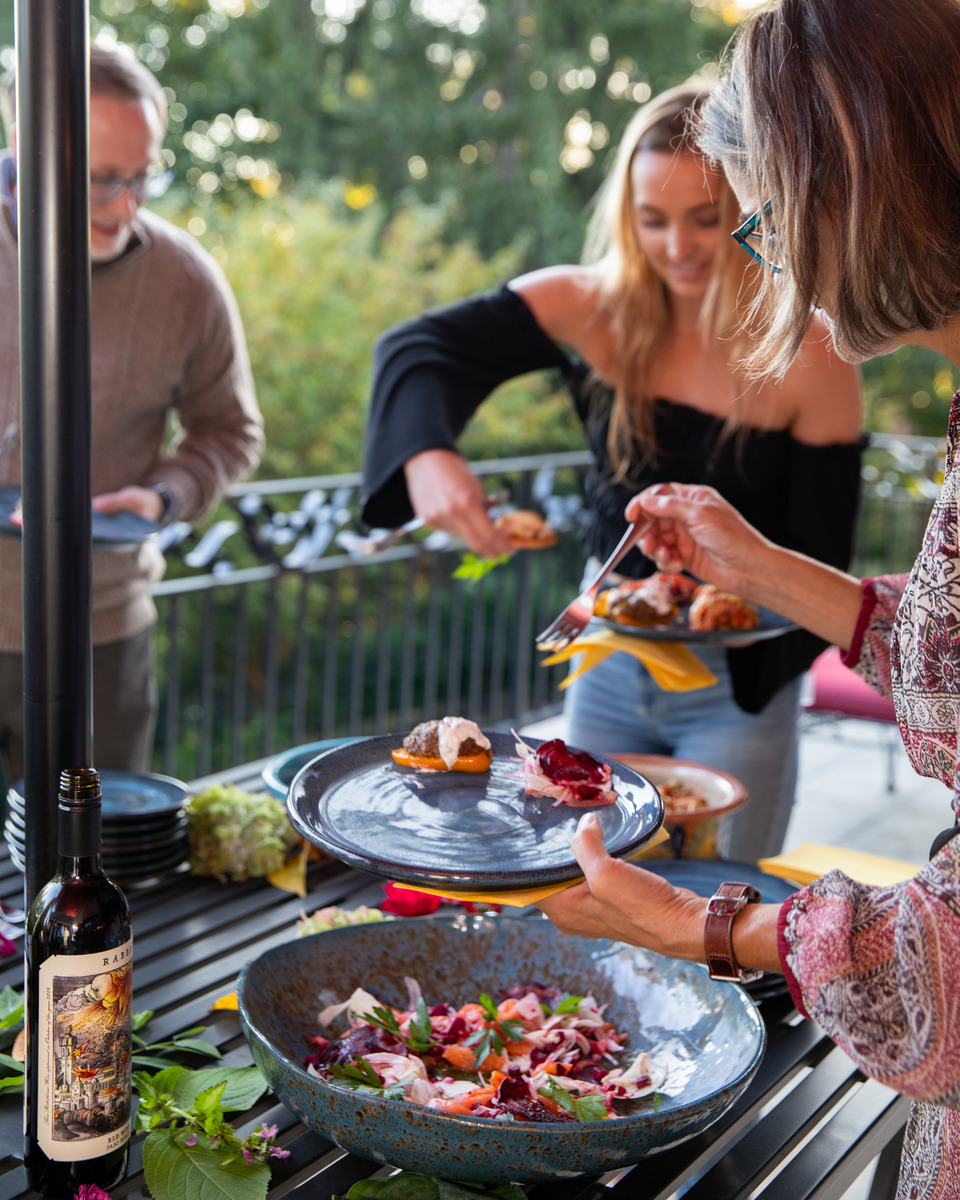 A group of people enjoying a meal outdoors on a patio, surrounded by lush greenery.
