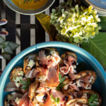 A plate featuring slices of toasted sourdough bread topped with thin slices of prosciutto, dollops of apple butter, shredded aged cheddar cheese, and drizzles of balsamic glaze and olive oil.