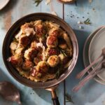 A plate of chicken meatballs in creamy orzo, staged on a white table.