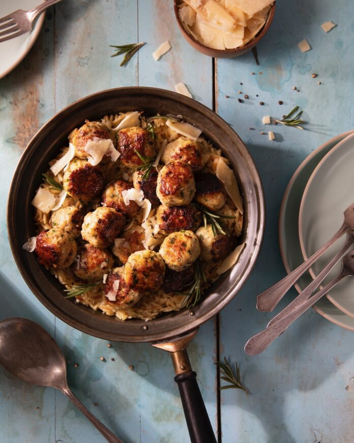 A plate of chicken meatballs in creamy orzo, staged on a white table.